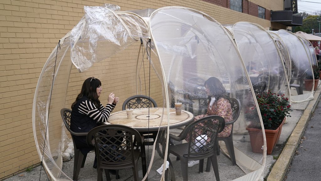 FILE - Aviva Markowitz, left, and Rivka Alter enjoy a drink in a protective bubble at the Lazy Bean Cafe in Teaneck, N.J., Thursday, Oct. 22, 2020. On March 11, 2024, an independent report examining New Jersey's response to the pandemic said the state and nation were unprepared for it, adding the state is still underprepared for the next crisis. (AP Photo/Seth Wenig, File)