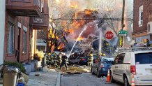 Flames engulf multiple row homes in South Philadelphia, with debris scattered on the street, as firefighters battle the blaze.