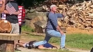 A man kneels on another man's back with flags near him