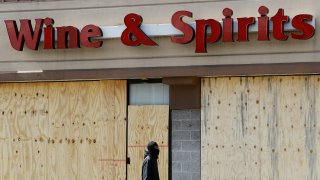 A pedestrian walks past a boarded up Wine and Spirits store, March 18, 2020, in Upper Darby, Pennsylvania. The state has shut down all of its roughly 600 state-owned wine and liquor stores to try to slow the spread of the new coronavirus.
