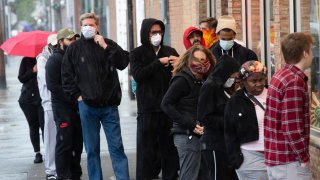 Shoppers wearing masks and face coverings wait in line to enter a store on South 9th Street in Italian Market neighborhood of Philadelphia, Thursday, April 9, 2020.