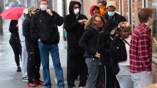 Shoppers wearing masks and face coverings wait in line to enter a store on South 9th Street in Italian Market neighborhood of Philadelphia, Thursday, April 9, 2020.