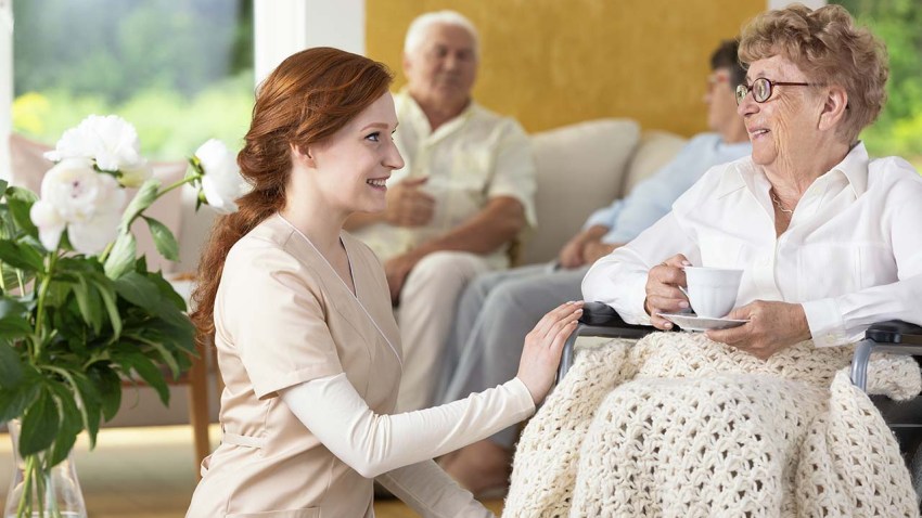 Smiling nurse taking care of disabled senior woman in the nursin