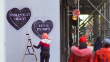 Woman artist with ladder putting up black and white heart art on white wall