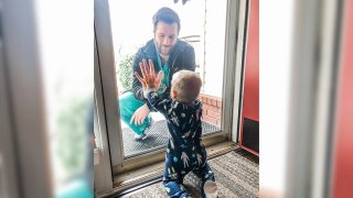 Dr. Jared Burks, sees his 1-year-old son crawl for the first time, as he touches a glass door from the outside while their son Zeke touches it from the inside of their Jonesboro, Ark.