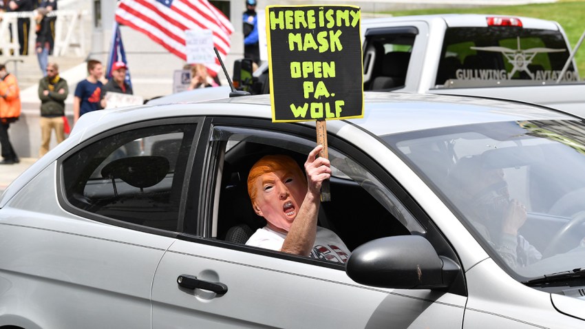 A car passenger disguised behind a Trump mask wields a sign as part of a "reopen" Pennsylvania demonstration on April 20, 2020, in Harrisburg, Pennsylvania.