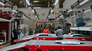 Tesla employees work to finish the upper rear trunk of the Tesla Model 3