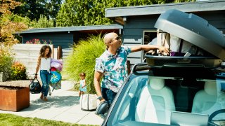 Family loading luggage into car top box before a road trip