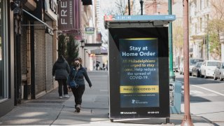 A person wearing a protective mask passes a sign about the stay at home order in downtown Philadelphia, Pennsylvania