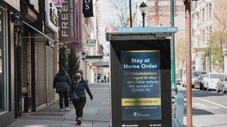 A person wearing a protective mask passes a sign about the stay at home order in downtown Philadelphia, Pennsylvania