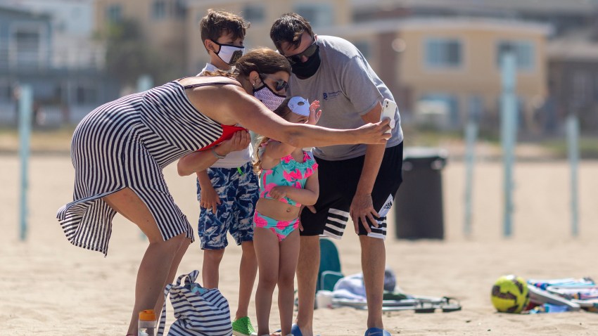 A family takes a group selfie in masks as people visit one of Los Angeles County's recently reopened beaches during the coronavirus pandemic, in Manhattan Beach, California on May 17, 2020.