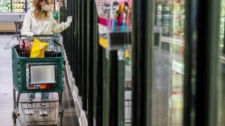 A young woman wearing a protective mask and gloves shopping in a time of virus pandemic, buying food supplies - processed frozen foods.