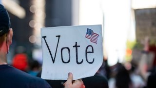 In this June 14, 2020, file photo, a protester holds a sign that says "Vote" with an American Flag as they march through the streets of New York City.