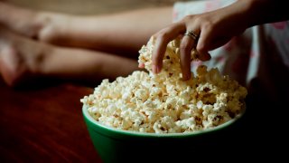 Woman hand into bowl filled with popcorn and her feet up on couch.