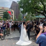 couple in tuxedo and wedding dress with protesters nearby