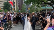 couple in tuxedo and wedding dress with protesters nearby