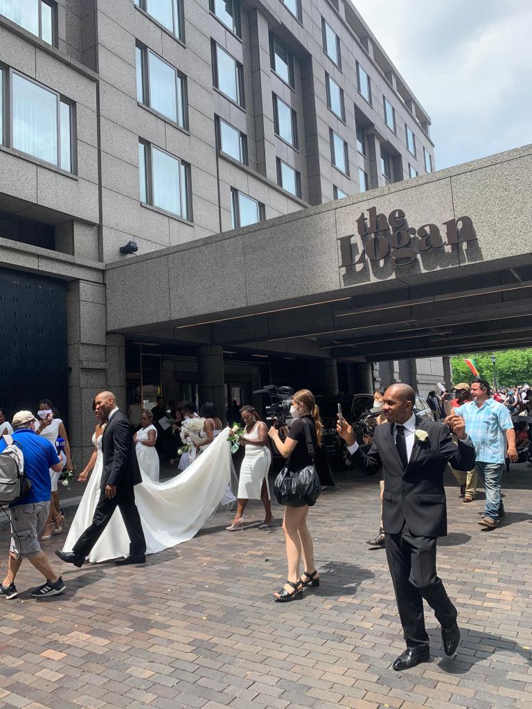 photographers and wedding party outside hotel, protesters with signs in background