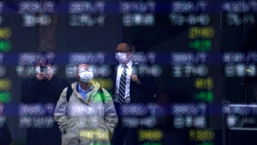 In this March 13, 2020, file photo, people are reflected on an electronic stock board showing Japan's Nikkei 225 index at a securities firm in Tokyo.