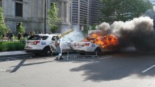 A woman is seen holding a piece of wood as a Philadelphia Police Department car burns in front of Philadelphia City Hall.