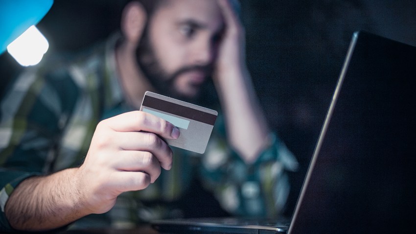 Close-up of a man paying bills from home by using a laptop and a credit card