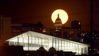 In this Wednesday, April 8, 2020 photo, the super moon rises behind the state Capitol in Denver.