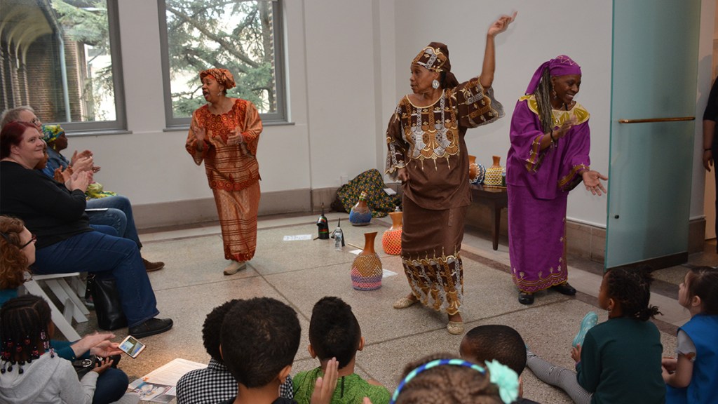 Women dancing in outfits from African culture in front of a crowd of children.