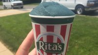 A hand holds up a cup of green water ice from Rita's Italian Water Ice