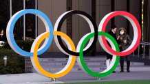 In this Feb. 27, 2020, file photo, visitors wearing face masks stand next to the Olympic Rings monument in front of the Japan Olympic Committee headquarters near the new National Stadium, venue of the Opening and Closing Ceremony of the Tokyo Olympic Games, in Tokyo, Japan.
