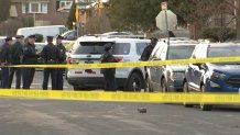 Philadelphia police officers stand behind yellow crime scene tape.