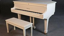 A white lacquered baby grand piano with a matching white bench. The piano has brass fittings and pedals.