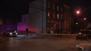 Philadelphia police officers use flashlights behind crime scene tape after a shooting.