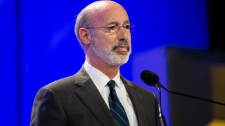 Gov. Tom Wolf stands at a lectern and in front of a microphone.