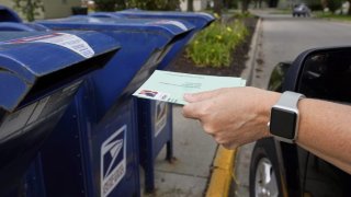 A person drops applications for mail-in-ballots into a mail box in Omaha, Neb