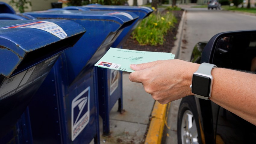 A person drops applications for mail-in-ballots into a mail box in Omaha, Neb