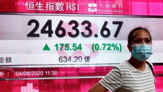In this Aug. 4, 2020, file photo, a woman wearing a face mask stands by a bank's electronic board showing the Hong Kong share index at Hong Kong Stock Exchange.