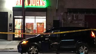 A van is parked in front of a Papa John's pizzeria and behind crime scene tape at the site of a deadly drive-by shooting.