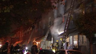 Smoke billows from a South Philadelphia row home as firefighters douse water on the fire.