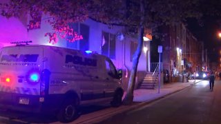 A Philadelphia Police Department van is parked on the sidewalk in front of a row home on a block where two Temple University students fell off a roof.