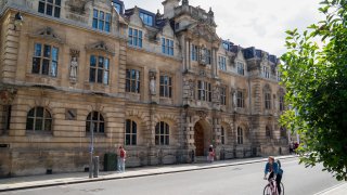 Pedestrians and a cyclist pass Oriel College, where a statue of Cecil Rhodes stands above an entrance, at the University of Oxford in Oxford, U.K., on Monday, July 20, 2020.