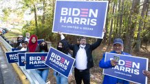 Gwinnett county voters including Menar Hague (C) wave Biden-Harris campaign signs at the entrance to Lucky Shoals Park polling station on November 3, 2020 in Norcross, Georgia.