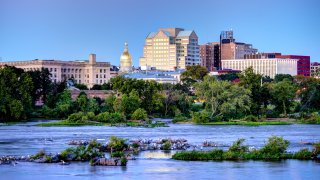 The skyline of Trenton, New Jersey, is shown behind a river.