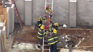 A man lays on a stretcher as firefighters surround him and help pull him up a ladder after the man was hurt from a fall into an open basement.