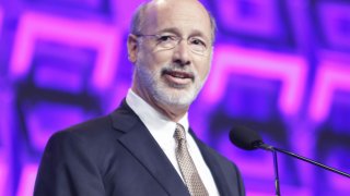 Governor of Pennsylvania Tom Wolf stands at a podium in front of a microphone and speaks on stage