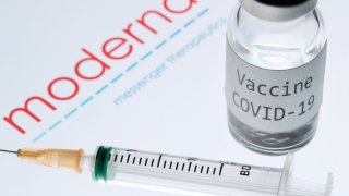 This picture taken on November 18, 2020 shows a syringe and a bottle reading “Vaccine Covid-19” next to the Moderna biotech company logo.