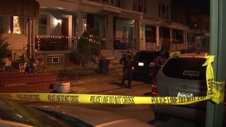 Crime scene tape surrounds a group of row homes in West Philadelphia as a police officer walks by following a fatal triple shooting.