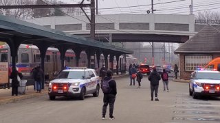Passengers stand around as two police SUVs park near a SEPTA station where a train is halted following a crash that killed a man.