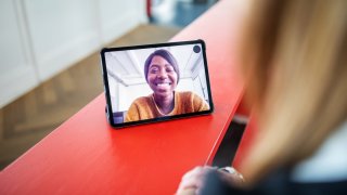 A woman is seen smiling through a tablet screen.