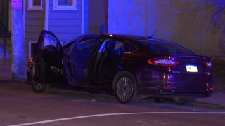 A dark-colored sedan is parked with its doors open near a sidewalk in the Mantua neighborhood of Philadelphia. Police say two women and a man were shot as they sat in the car.