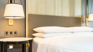 A lamp is turned on next to a made hotel bed