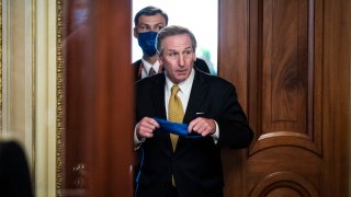 Michael van der Veen, lawyer in former President Donald Trump's impeachment trial, raises a blue face mask toward his face as he walks between two wooden doors. A man walks behind him, already wearing a face mask.